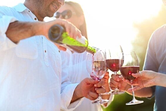 Closeup of people clinking their wine glasses filled with red wine together.
