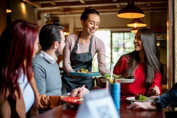 A smiling waitress serves food to three people sitting at a table in a restaurant.