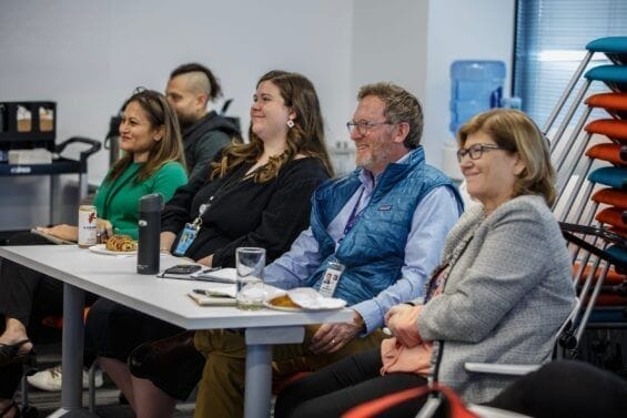 A row of smiling people sit at a desk while attending a workshop.