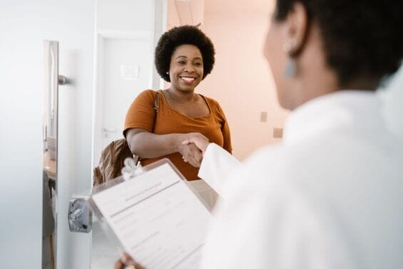 A smiling woman shakes hands with a doctor holding a clipboard.