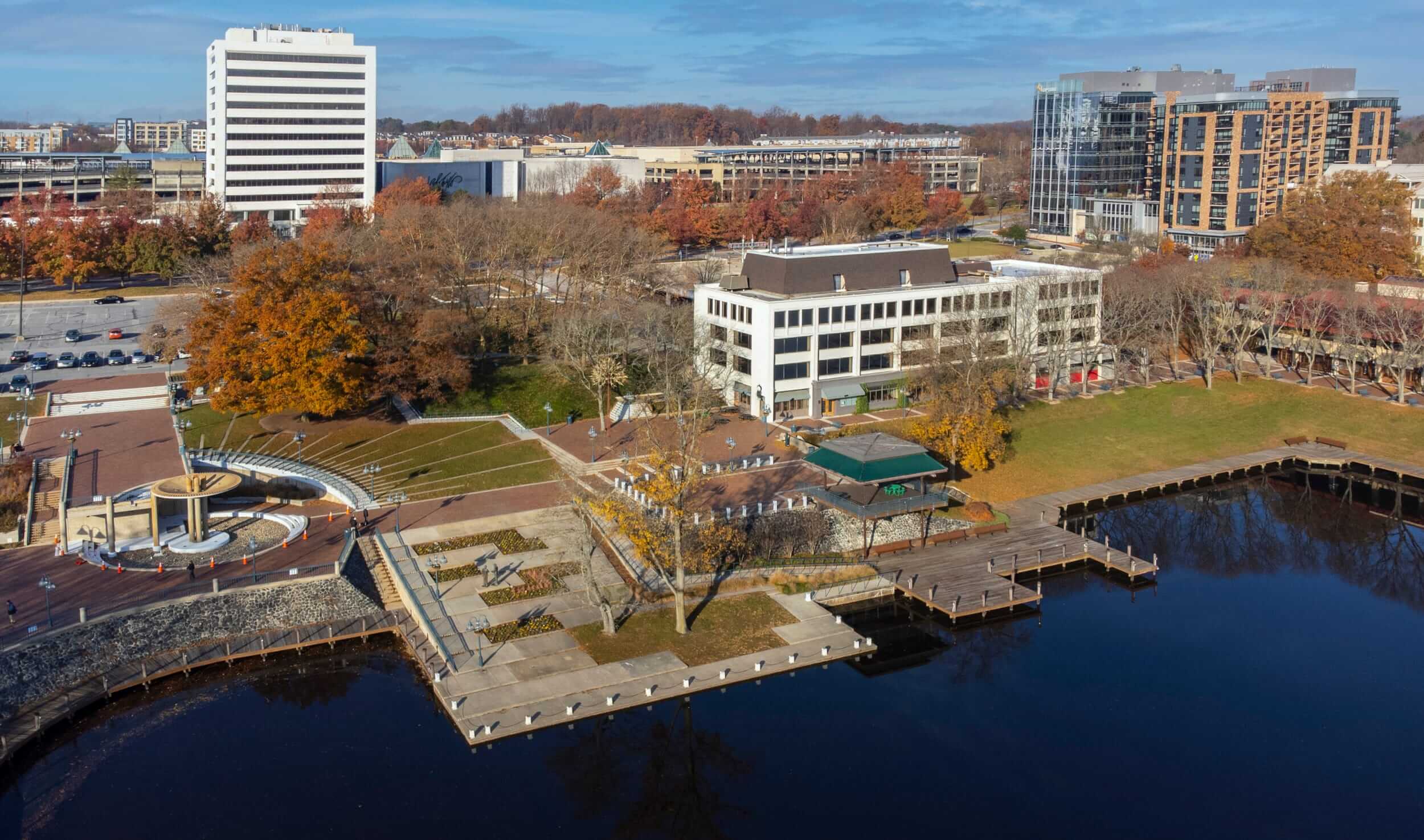 An aerial shot of a lakefront dock with a park, building and autumn trees along the shore.