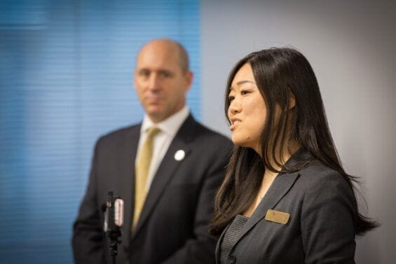 An Asian businesswoman speaks while a businessman listens from the side.
