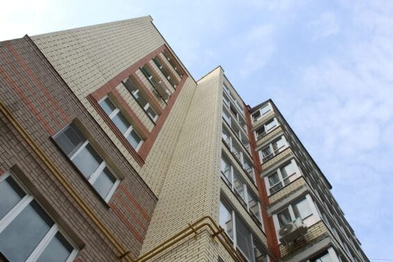 An apartment building seen from the bottom up rises against a blue sky.