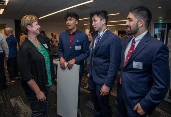 A diverse group of businessmen speak with a businesswoman in a classroom.